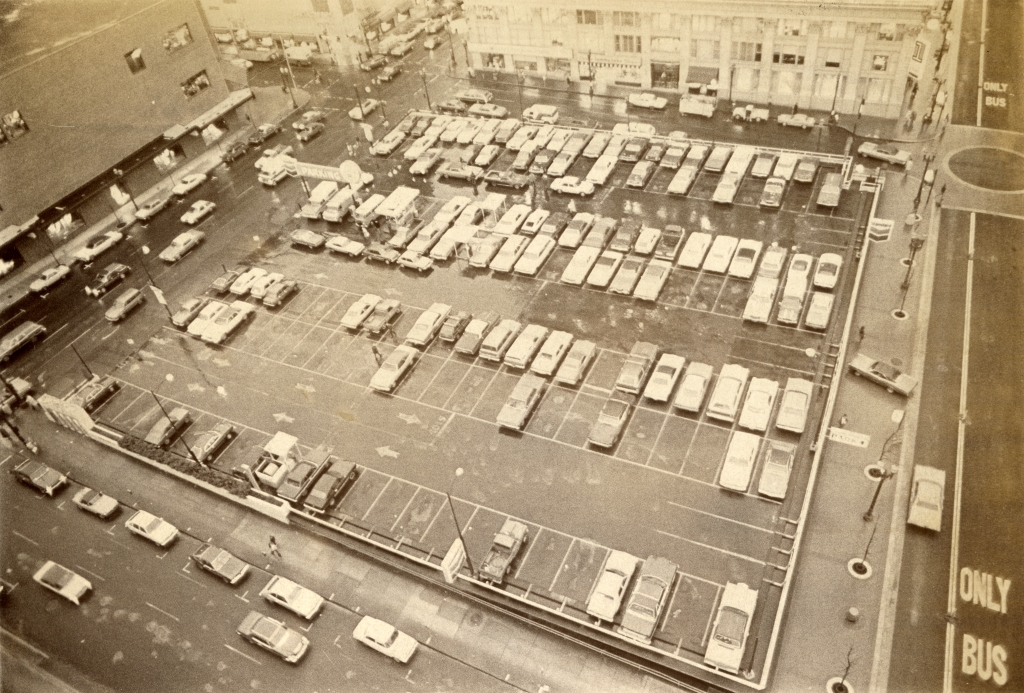 Aerial view of the parking garage with several cars parked. The lot is surrounded by streets and buildings. 